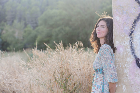 Portrait of a beautiful young woman with long brown hair in a blue dress standing in the field.の写真素材