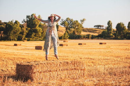 Beautiful woman sitting on a haystack in a wheat field.の写真素材