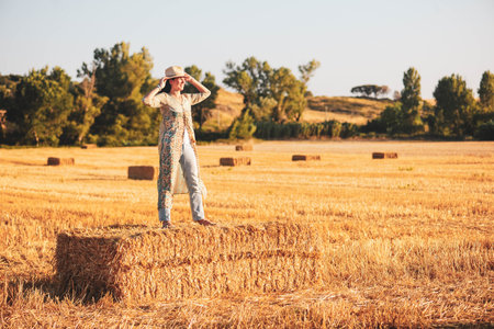 Beautiful woman sitting on a haystack in a wheat field.の写真素材