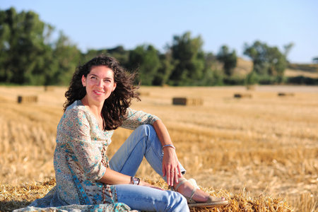 Beautiful woman sitting on a haystack in a wheat field.の写真素材