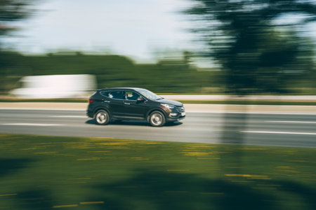 A dark SUV drives along an asphalt road in the summer among the greeneryの写真素材