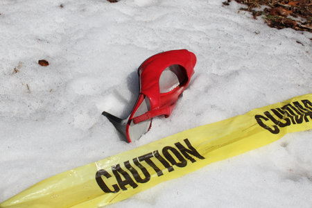 A red high heel in the snow by caution tape.の写真素材