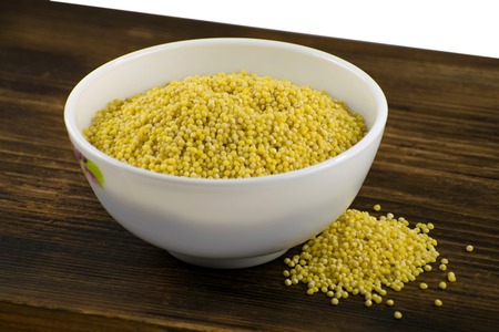 Millet in white bowl on brown board. Healthy dietary groats background.