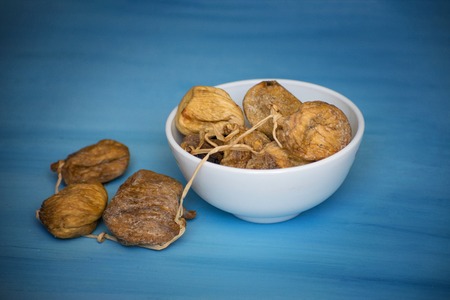 Dried figs in a white bowl on a blue table.
