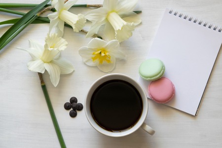 Notepad, macarons, cup of coffee and daffodils on a white table.の写真素材