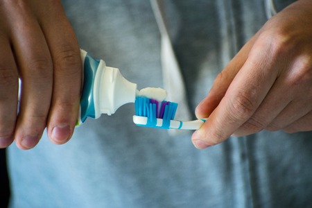 A close-up of a young man's hands is holding a toothbrush and putting a toothpaste on her.の写真素材