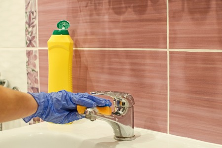 Cleaning bathroom sink with cleaning agent. Woman cleans the faucet in the bathroom.の写真素材
