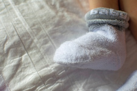 Newborn baby feet close up. Baby feet in white terry socks, baby lying on bed, baby's legs,の写真素材