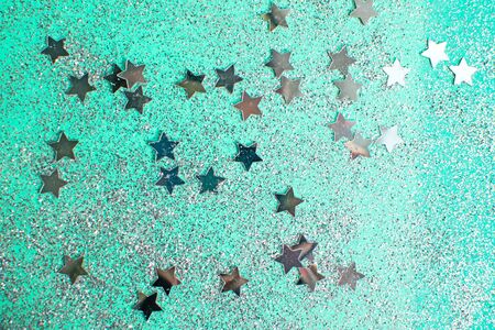 Splash of silver sparkles and stars on mint background. Blurry image. Selective focus.