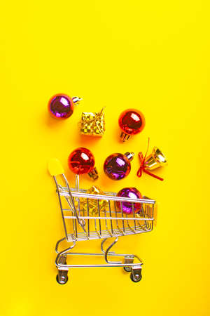 Shopping cart full of christmas balls, gifts and sparkling bells on a yellow background.の写真素材