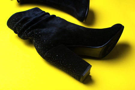 Women's black boots from natural suede on a yellow background. Black boots with rhinestones. Fashionable concept.の写真素材