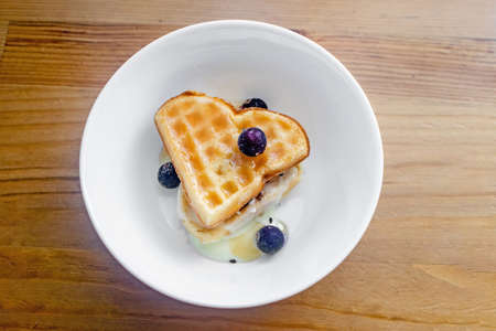 Tasty homemade Belgian waffles heart shaped on white bowl with berries and condensed milk.の写真素材