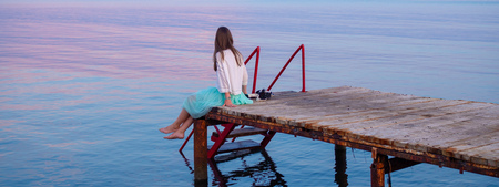 Side view of a wooden pier on the sea at sunset with young woman sitting on it, admirring amazing sunset, Durres, Albania. Awesome sunset skyの写真素材