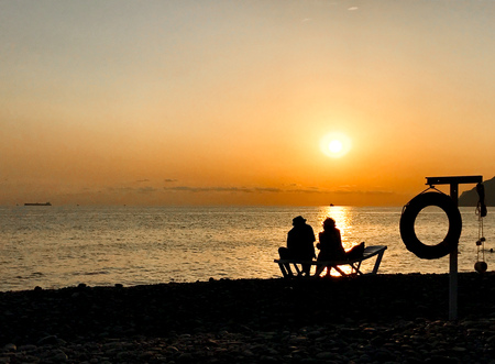 Golden sunset on the ocean shore and sand. Couple of people admiring the sunset.の写真素材