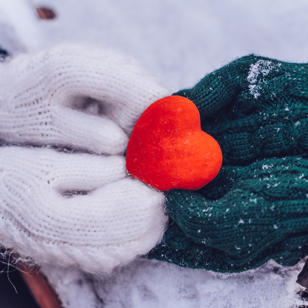 Hands in gloves holding heart closeup on winter snow background. Toned. Valentines Day and love concept, squareの写真素材