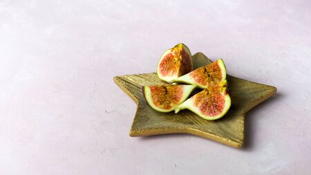 Arrangement of fresh cut figs on golden wooden plate on light pink background, copy space, banner. Selected focusの写真素材