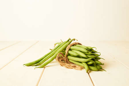 bunch of raw green beans tied up with a string on white wooden tableの写真素材