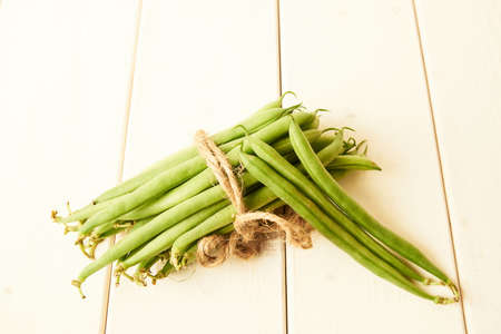 bunch of raw green beans tied up with a string on white wooden tableの写真素材