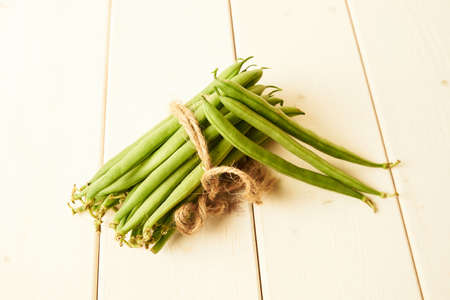 bunch of raw green beans tied up with a string on white wooden tableの写真素材