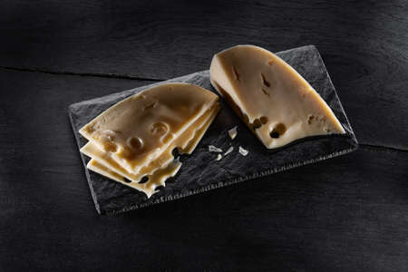 slices of cheese on a slate board on a dark backgroundの写真素材