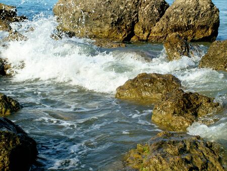 bubbling waves on a rocky pebble sea shore in the afternoon in summerの写真素材