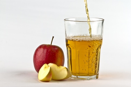 Apple cider pouring down into glass with apples at the side. On white backgroundの写真素材