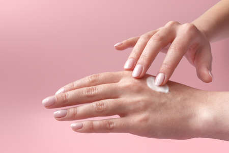 Female hands on light pink background. Cold season hands skin protection. Closeup woman applying...