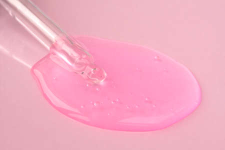 Pipette with fluid hyaluronic acid on pink background. Cosmetics and healthcare concept closeup. Dose of serum or retinol with air bubbles. Flat lay. Luxury gel or beauty product presentation in macroの写真素材