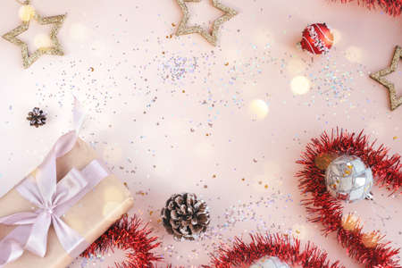 Christmas or New Year festive background with space for text. Present in kraft paper with pink ribbon on soft beige background with glitter, stars, balls, confetti, tinsel. Xmas composition. Flat layの写真素材