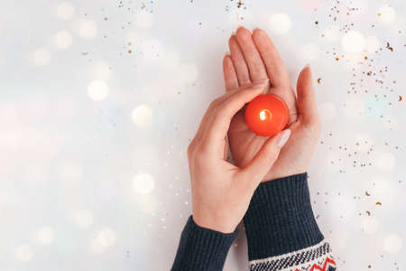 Female hands in sweater holding red candle with flame. Winter holiday, Christmas, Valentines day...