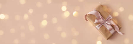 Banner of birthday or New Years eve present in kraft paper with pink ribbon on soft beige background with bokeh lights. Xmas composition. Flat lay. Happy holidays celebration and giving love conceptの写真素材