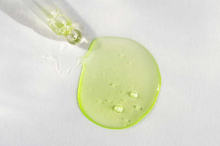 Pipette with green hyaluronic acid on white background. Cosmetics and healthcare concept closeup. Dose of serum or retinol with air bubbles. Top view. Luxury gel or beauty product presentation, macroの写真素材