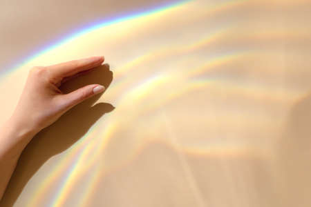 Female hand with sun refraction on beige background. Overlay mode. Caustic effect of light. Shadows texture. Blurred water backdrop. Multicolored sun reflections. Trendy concept of technology, scienceの写真素材