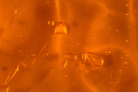 Texture of transparent yellow gel with air bubbles and waves on orange background. Concept of skin...