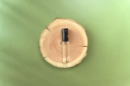Beige woodcut disk lying on a trendy green background with flower shadows and transparent glass perfume tester. A platform made of tree for luxury and natural cosmetics presentation. Wood tray mockupの写真素材