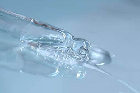 Pipette with fluid hyaluronic acid on blue background. Cosmetics and healthcare concept closeup....