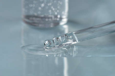 Pipette with fluid hyaluronic acid on blue background. Cosmetics and healthcare concept closeup. Dose of serum or retinol with air bubbles. Flat lay. Luxury gel or beauty product presentation in macroの写真素材