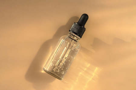 Transparent glass dropper bottle with air bubbles on beige background in sunlight. Pipette with fluid hyaluronic acid, serum, retinol. Cosmetics and healthcare concept Flat lay. Luxury beauty productの写真素材