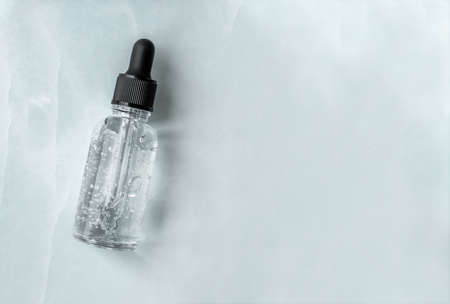 Transparent glass dropper bottle with air bubbles on marble background. Pipette with fluid hyaluronic acid, serum, retinol or oil. Cosmetics and healthcare concept. Flat lay. Luxury beauty productの写真素材