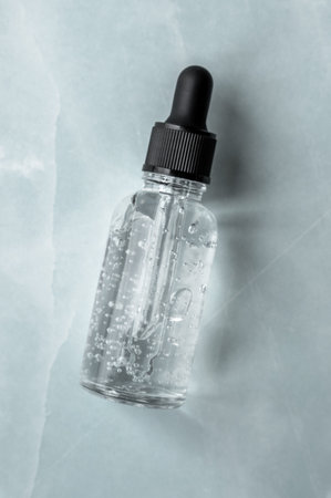 Transparent glass dropper bottle with air bubbles on marble background. Pipette with fluid hyaluronic acid, serum, retinol or oil. Cosmetics and healthcare concept. Flat lay. Luxury beauty productの写真素材