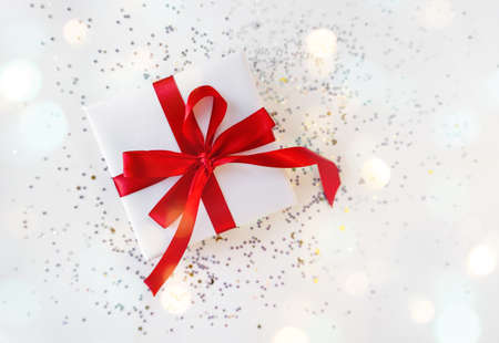 Gift box wrapped in white paper with a red bow on festive light background. Copyspace for your text. Flat lay style. Christmas, New Year or birthday celebration concept. Web element for postcardの写真素材