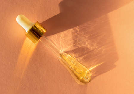 Pipette with fluid hyaluronic acid on a trendy beige background in sunlight. Cosmetics and healthcare concept closeup. Dose of serum or retinol. Luxury gel or beauty product presentation in macroの写真素材