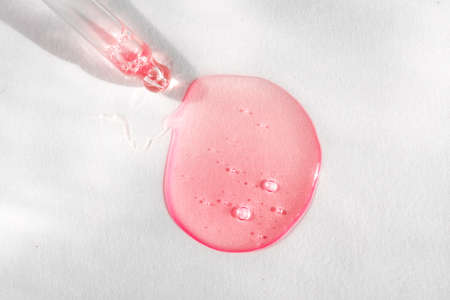 Pipette with pink fluid hyaluronic acid on white background. Cosmetics and healthcare concept. Dose of serum or retinol with air bubbles. Flatlay. Luxury gel or beauty product presentation in macroの写真素材