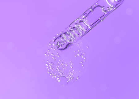 Pipette with fluid hyaluronic acid on violet background. Cosmetics and healthcare concept closeup. Dose of serum or retinol with air bubbles. Flat lay. Luxury beauty product presentation in macroの写真素材