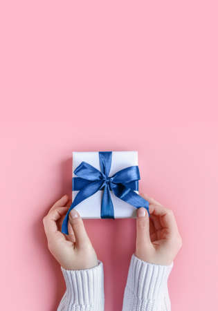 Female Hands in sweater holding gift in white wrapping paper on pink background. St. Valentines Day, love, tenderness, friendship, Birthday, Christmas, care concept. Cozy, festive, romantic wallpaperの写真素材