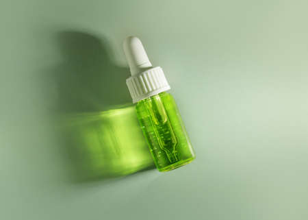 Transparent glass dropper bottle with green liquid inside on lemon mint background in the sunlightt....