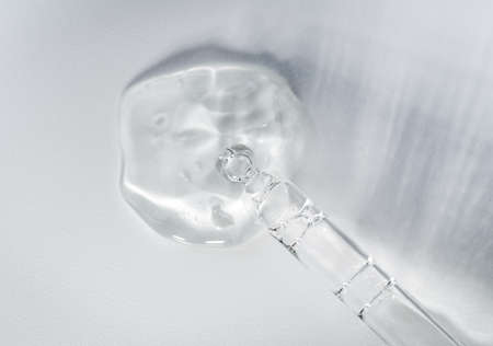 Pipette with fluid hyaluronic acid on gray background. Cosmetics and healthcare concept closeup....