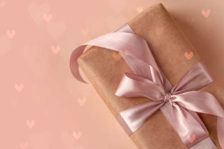 Valentines Day, Birthday or New Year present in kraft paper with pink ribbon on soft beige...