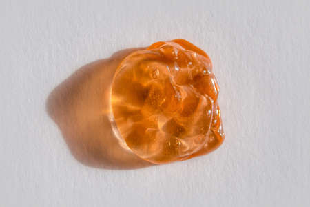 Orange cosmetics or antiseptic gel, cleaner, or serum drop on gray background. Colorful amber slime with air bubbles in the sunlight. High contrast trendy photo. Health protection conceptの写真素材