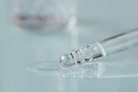 Pipette with fluid hyaluronic acid on blue background. Cosmetics and healthcare concept closeup. Dose of serum, retinol with air bubbles. Flat lay. Luxury beauty product presentation, macroの写真素材